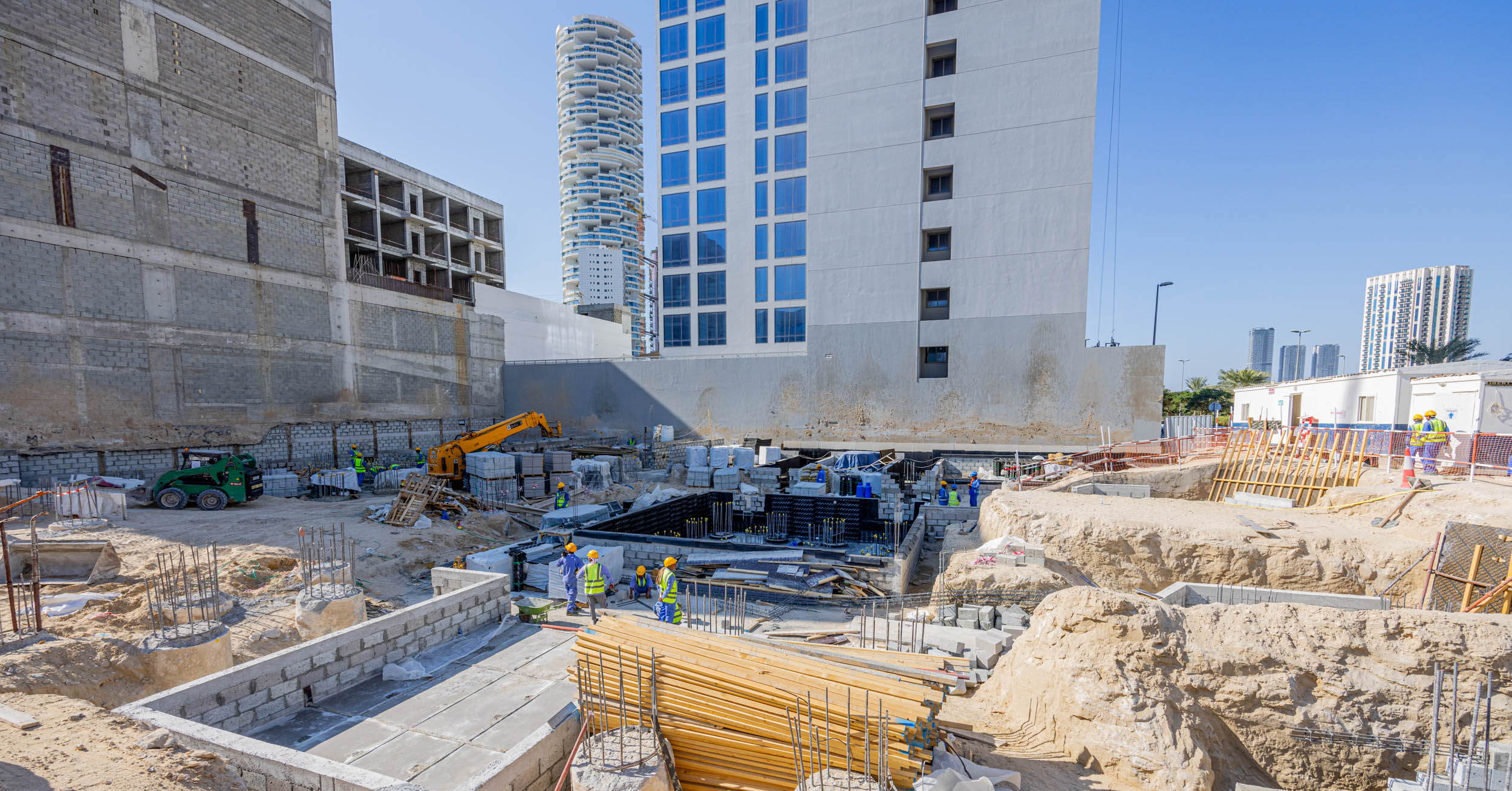 Pearl House By Imtiaz Construction site with workers, machinery, and materials in a developing urban area under clear blue skies.